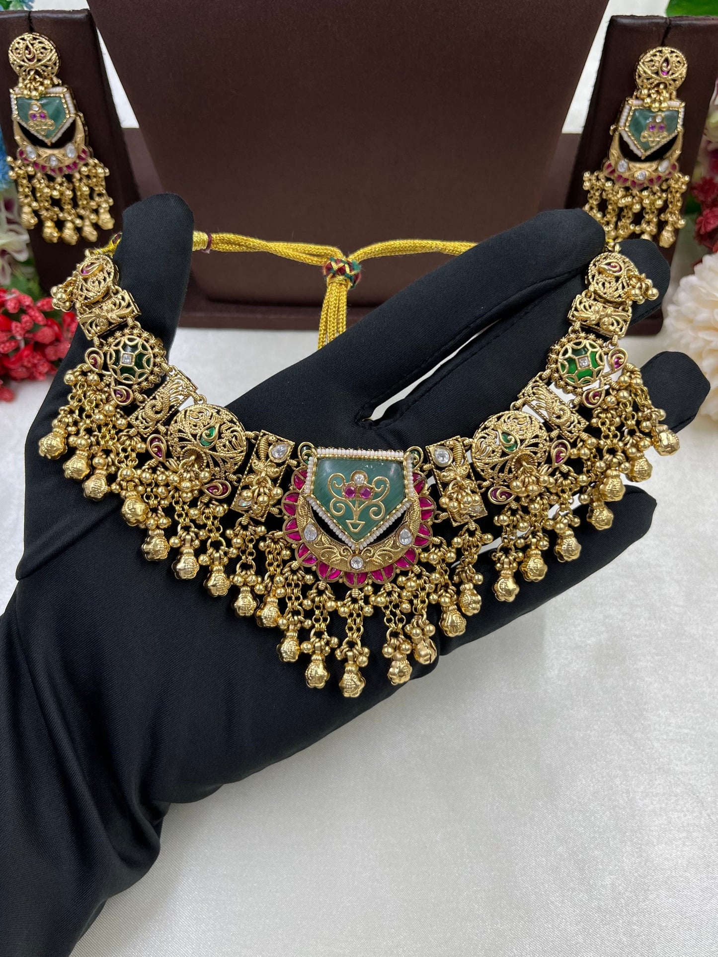Gold necklace with green and red accents on a black stand