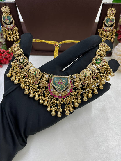 Gold necklace with green and red accents on a black stand